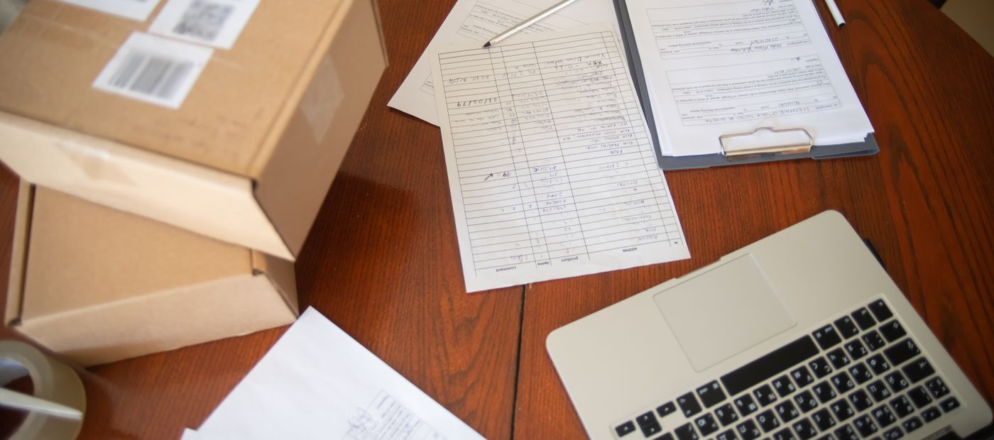 Cardboard boxes, a packing list and a laptop on a wooden desk