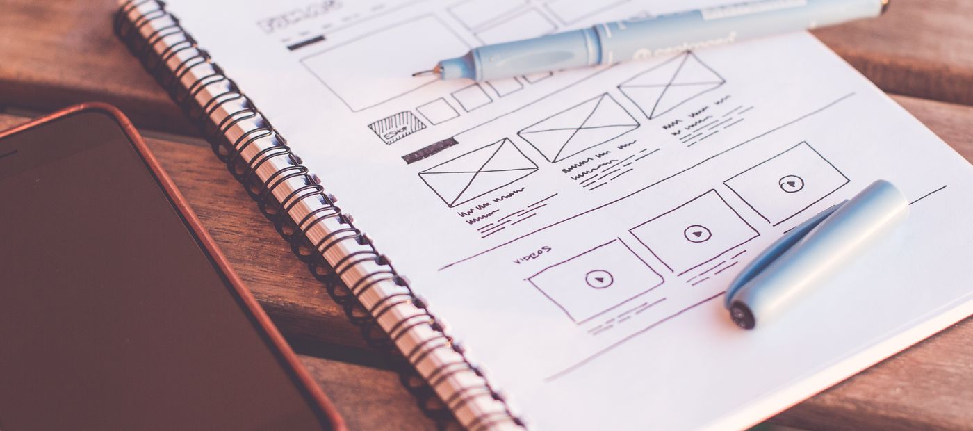 A notebook of interface sketches beside a smartphone on a desk
