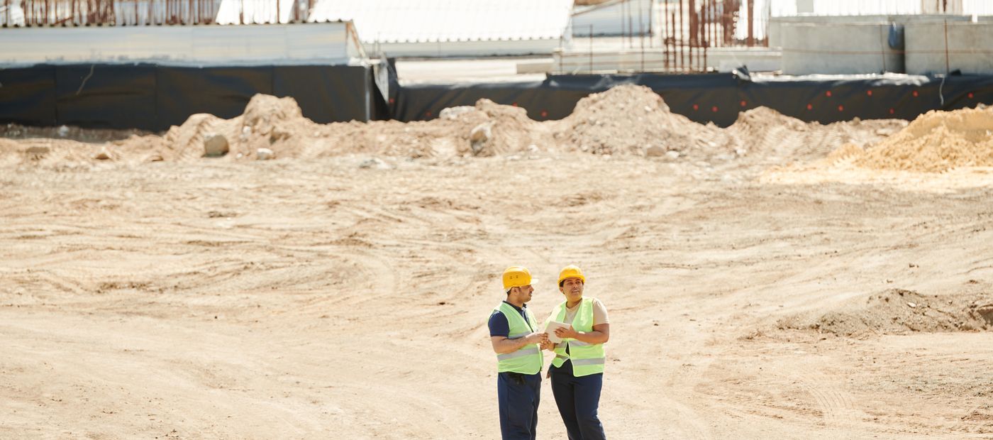 Two workers in safety gear discussing plans on a construction site