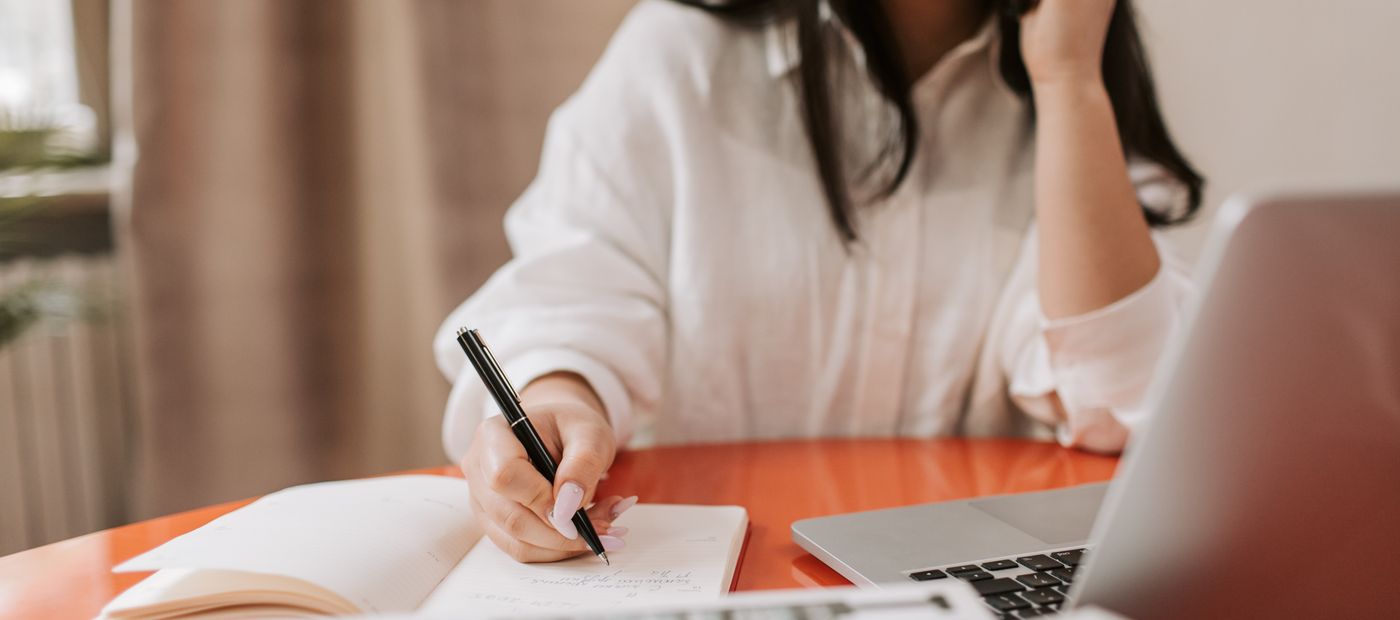 Somebody at a desk writing notes during a phone call, laptop open
