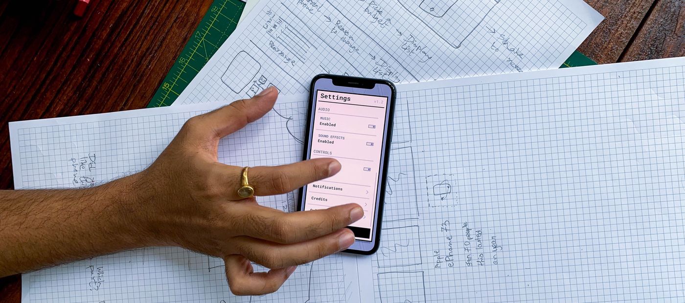 A hand holding a phone over app design sketches on paper
